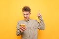 Portrait of a bewildered nerd boy in glasses and shirt uses a smartphone and looks at the screen with weary face, pointing his Royalty Free Stock Photo