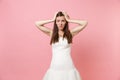 Portrait of bewildered puzzled bride woman in lace white wedding dress worries clinging to head standing isolated on