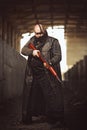 Portrait of big brutal man with rifle in leather coat as Mad Max style at abandoned building