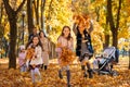 Portrait of big family in autumn city park, children running with armful of leaves, happy people playing together and scattering