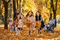 portrait of big family in autumn city park, children running with armful of leaves, happy people playing together and scattering