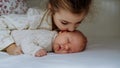 Portrait of big sister cuddling newborn, little baby. Girl kissing her sleeping new sibling in bed. Sisterly love, joy