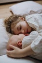 Portrait of big sister cuddling newborn, little baby. Girl lying with her new sibling in bed. Sisterly love, joy for new
