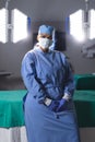 Portrait of biracial female surgeon wearing surgical gown and face mask in operating theatre Royalty Free Stock Photo