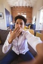 Portrait of biracial young man blowing air kiss on virtuality date at home