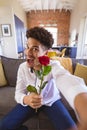 Portrait of biracial young man with rose enjoying virtual date at home