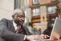Portrait of black african american businessman in suits sits at a table in a summer cafe with a laptop outdoors Royalty Free Stock Photo