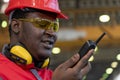 Black Worker In Protective Workwear Talking On Radio Communication Equipment In A Factory