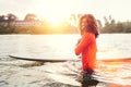 Portrait of black long-haired teen boy with surfboard ready for surfing with sunset backlight. He walking in Indian ocean waves.