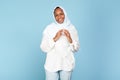Portrait of black muslim woman joining fingers together while posing over blue studio background and smiling to camera Royalty Free Stock Photo
