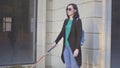 A blind woman wearing glasses with a cane walking in front of shop windows