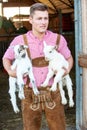 Blond bavarian man holding two little white goats Royalty Free Stock Photo