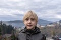 Portrait of blond boy in black jacket on the mountains background. Fair-haired teenager outside. Schoolboy walks outside