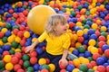 Portrait of a blond boy in a yellow t-shirt. The child smiles and plays in the children`s playroom. Ball pool Royalty Free Stock Photo