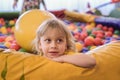 Portrait of a blond boy in a yellow t-shirt. The child smiles and plays in the children`s playroom. Ball pool