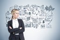 Portrait of a blond businesswoman standing with crossed arms near a gray wall.