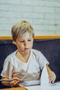 Portrait blond cute Preschool boy holding pen leafing through notebook look serious thoughtful think tired learn write