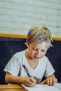 Portrait blond cute Preschool boy holding pen notebook look happy learn write, artistic facial expressions gestures