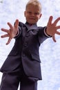 Portrait of a blond first-grader boy dressed in a dark suit with his arms outstretched to the camera, view from above.