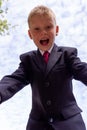 Portrait of a blond first-grader boy dressed in a dark suit with his arms outstretched to the camera, view from above.