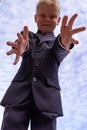 Portrait of a blond first-grader boy dressed in a dark suit with his arms outstretched to the camera, view from above.