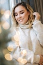 Portrait of blond hair woman in hoodie open present on Chrisrmas time. Elegant woman stand by big Christmas tree in Royalty Free Stock Photo