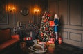 Portrait of blond woman with gift standing in dark living room near holiday Christmas tree Royalty Free Stock Photo