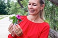 Blond woman outdoors holding a miniature watering can with a flower