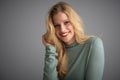 Portrait of blond young woman looking at camera and smiling while posing at light grey background Royalty Free Stock Photo