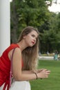 Portrait of blonde attractive young lady in elegant red dress on park background. Beautiful woman resting in park. Vertical frame Royalty Free Stock Photo