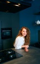 Portrait of blonde caucasian woman standing and smiling in her kitchen leaning on the table. Young cheerful adult female Royalty Free Stock Photo