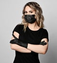Portrait of blonde curly woman in black t-shirt, mask and latex gloves stands holding arms crossed at chest