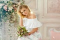 Portrait of a blonde girl with blue eyes in a summer dress sitting on the couch, holding flowers in her hand. Beauty Royalty Free Stock Photo