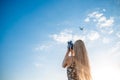 Portrait of a blonde girl in a floral print dress with a vintage video camera in a grape field records video of a plane taking off Royalty Free Stock Photo