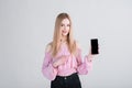Portrait of a blonde girl who shows the smartphone screen and points her finger at it in the studio on a white background. Royalty Free Stock Photo