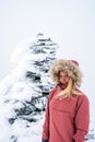 Portrait of blonde hiker girl with fur hooded jacket and backpack outdoors in the mountains with snow.