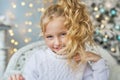 Portrait of blonde pretty little girl in white sweater on a chair in Christmas