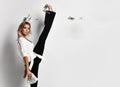 Portrait of blonde slim woman model in shirt and trousers with fan of dollars cash in hand doing vertical splits holding leg up