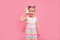 Portrait of blonde surprised child girl listen a seashell at the pink studio background. Summer vacation, ear diseases