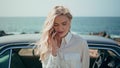 Portrait blonde talking smartphone standing beautiful sea coast near retro car. Royalty Free Stock Photo