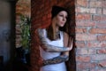 Portrait of a blonde tattoed girl dressed in white t-shirt and hat leaning on a brick wall in room with loft interior. Royalty Free Stock Photo