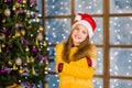 Portrait of blonde teen girl in red christmas hat on the background of Christmas tree Royalty Free Stock Photo