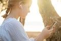 Portrait of blonde teenage girl in headphones holding mobile phone and standing sideways on the background of sea Royalty Free Stock Photo