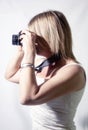 portrait of blonde woman with camera, intent on shooting, fair complexion dressed in light dress.