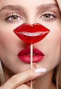 Portrait of blonde woman closes by candy her nose. Red female lips shape lollipop. Sweet tooth concept Royalty Free Stock Photo