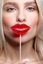 Portrait of blonde woman kissing candy. Red female lips shape lollipop. Sweet tooth concept