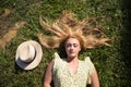 Portrait of blonde woman with long hair, young and beautiful farmer, lying on fresh green grass. Next to her a straw hat. The girl Royalty Free Stock Photo