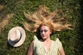 Portrait of blonde woman with long hair, young and beautiful farmer, lying on fresh green grass. Next to her a straw hat. The girl Royalty Free Stock Photo