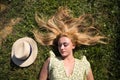 Portrait of a blonde woman with long hair, young and beautiful, lying on fresh green grass. Next to her a straw hat. The girl is Royalty Free Stock Photo