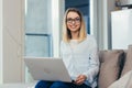 Portrait of a blonde woman looking at the camera sitting at home on the couch and holding a laptop Royalty Free Stock Photo